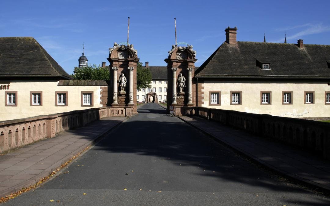 Ehemalige Benediktinerabtei Corvey bei Höxter, Nordrhein-Westfalen - Blick von der Brücke auf den Eingang zur Klosteranlage, rechts die Vorburg, die die Klosterkirche verdeckt (nur die beiden Turmspitzen ragen hinter dem Dach der Vorburg hervor). Durchs Tor sieht man einen Teil der Abtei.