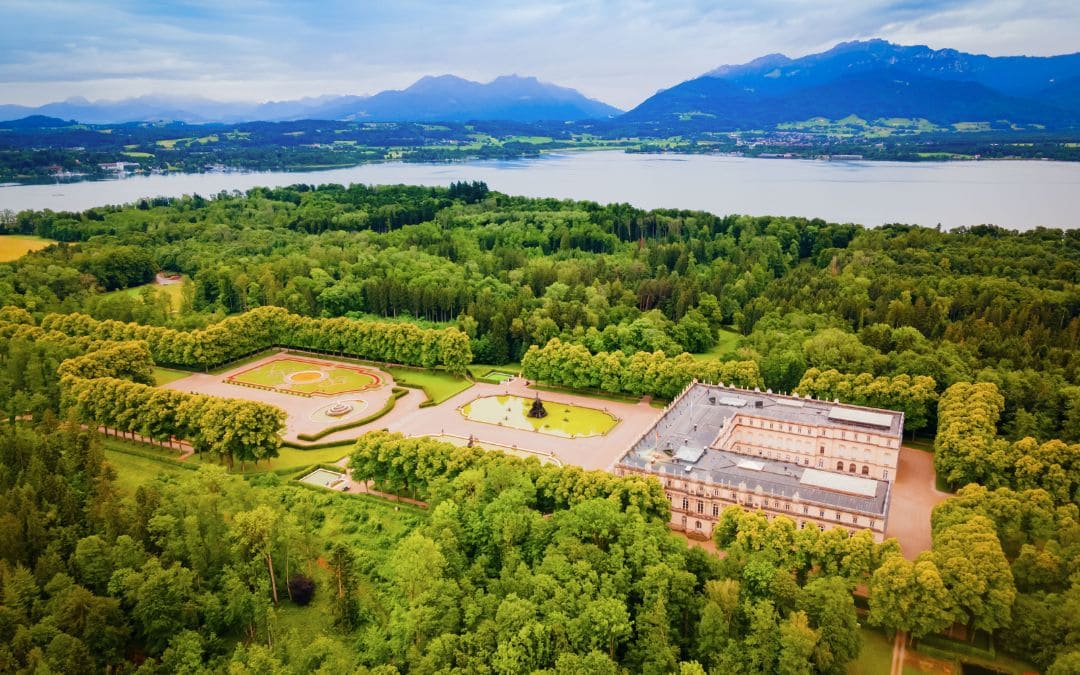 Schloss Herrenchiemsee, Bayern: Luftaufnahme des Schlosses, der umgebenden Anlagen und bewaldeten Inselfläche im Chiemsee, im Hintergrund die Bayerischen Alpen 