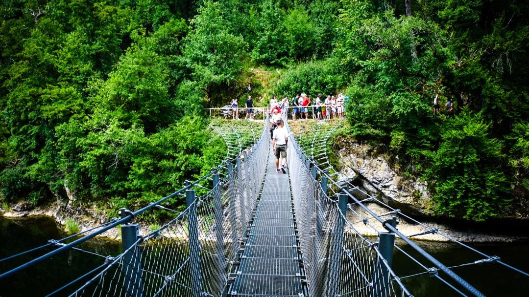 Fürstlicher Park Inzigkofen, Hängebrücke - Kinder und Erwachsene, die über die stählerne Hängebrücke gehen, von hinten fotografiert, auf der anderen Seite stehen viele Menschen und schauen auf die Brücke - angiestravel