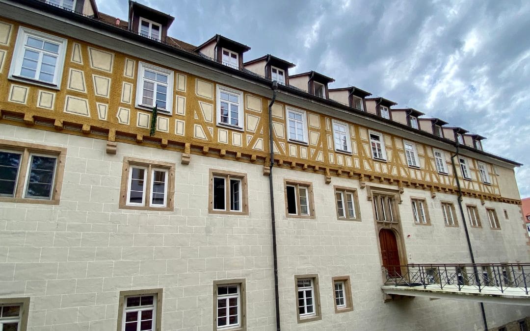 Tübingen, Evangelisches Stift - side view from the Neckarhalde - bridge with wrought-iron railing to the side entrance - lower part of the building sandstone masonry, upper floor yellow-painted half-timbering, small dormers at the top - angiestravelroutes.com