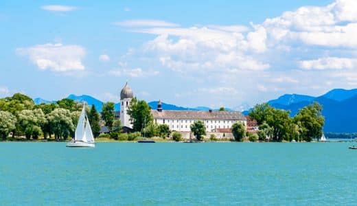 Chiemsee, Fraueninsel, Bavaria - View from the lake to the Fraueninsel with Frauenwörth Abbey, on the left in front of the island a sailing boat, in the background the Alps