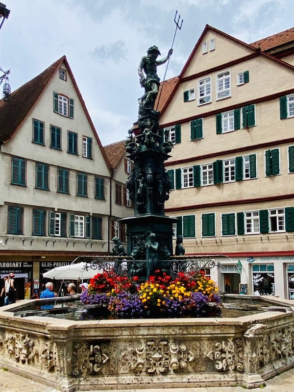 Tübingen, market square, Neptune Fountain - octagonal decorated shell limestone trough, richly decorated column with Neptune figure - colorful floral decoration of the city at the base of the column - angiestravelroutes.com