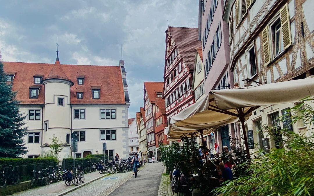 Tübingen, Collegiumsgasse - cafés and small stores in the row of half-timbered houses on the right, the Wilhelmsstift on the left, many parked bicycles in front - angiestravelroutes.com