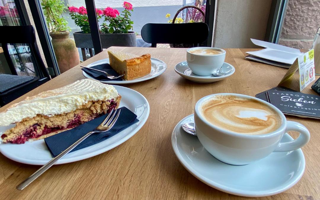 Weil der Stadt - Café Pfarrgasse Sieben - two plates with pieces of cake and two cups of cappuccino on a table, in the background a window with flowers planted in front of it - angiestravelroutes.com