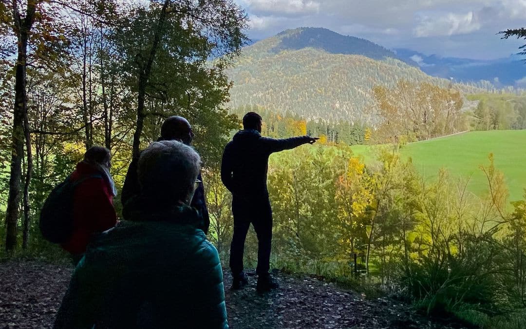 Standort Berghof, Obersalzberg, Berchtesgaden - Hannes Liebrandt steht vorne am Rand der Lichtung und deutet auf die Alpenlandschaft vor sich, mit etwas Abstand hinter ihm einige Personen, die im Schatten stehen - angiestravelroutes.com