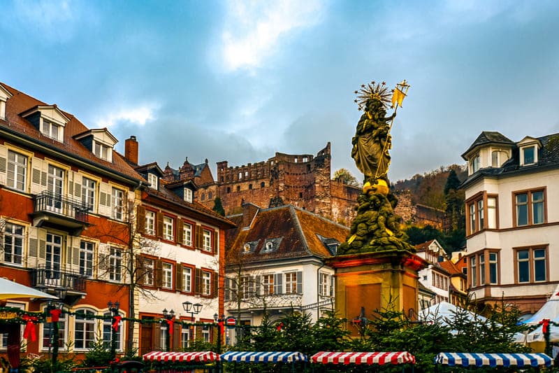 Heidelberg Christmas Market - Kornmarkt with statue of the Virgin Mary on the Mother of God Fountain, in the background the castle ruins - angiestravelroutes.com