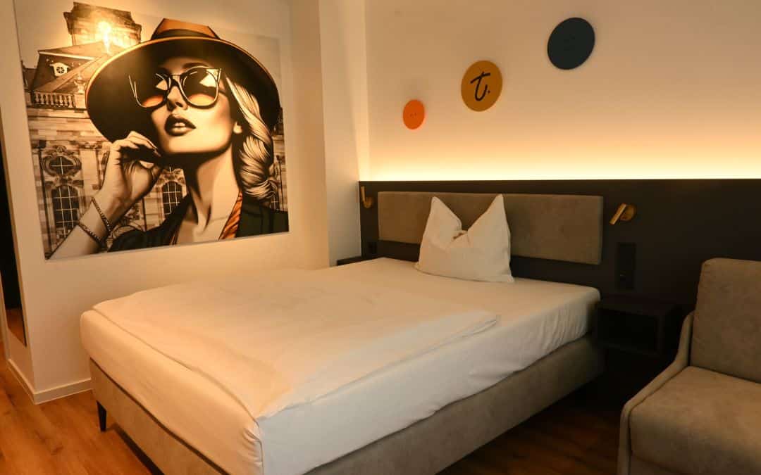 Hotel am Triller, Saarbrücken - Studio-Apartment, Boxspringbett, Wandbild im Pop-Art-Stil (großformatiges Porträt einer Frau mit Sonnenbrille und Hut, im Hintergrund die Ludwigskirche)