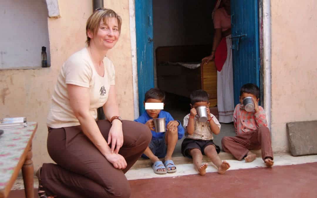 State of Uttar Pradesh, India - I am squatting next to three little boys on the floor of our driver's house, in the background a blue open door to one of the bedrooms, where a woman with a long dress is half hidden by the door - angiestravelroutes.com