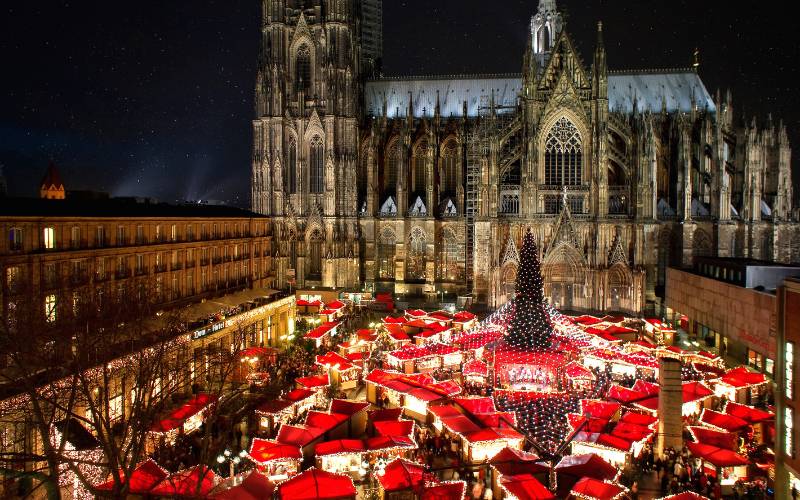 Cologne Christmas Market - Roncalliplatz with Christmas stalls and the Christmas tree covered with a net of LED lights in front of Cologne Cathedral. - angiestravelroutes.com