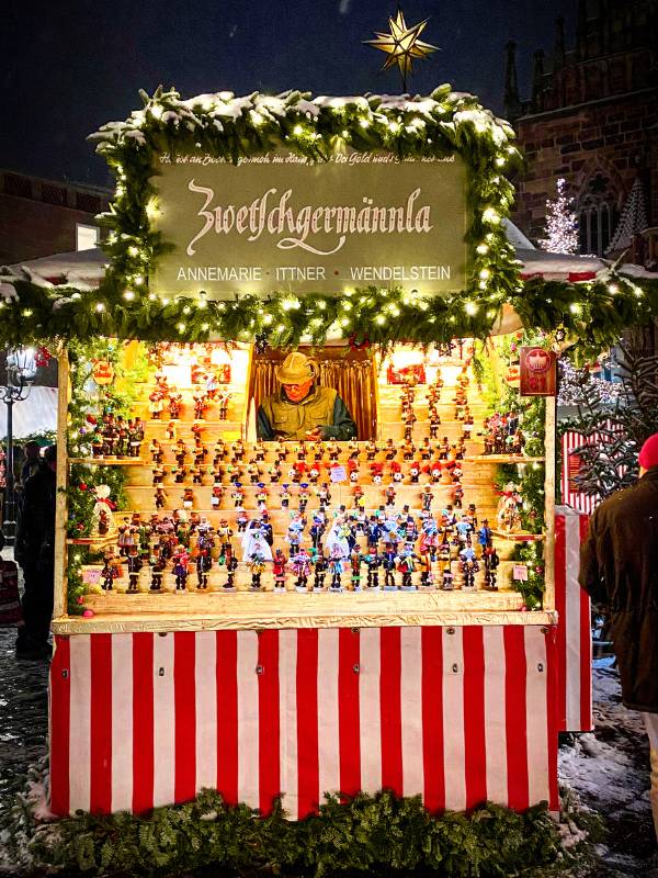 Nuremberg Christkindlesmarkt Zwetschgermännla stall - the market stall with many different Zwetgenmännla and the Verköufer at Nuremberg's main market in the evening with the typical red and white striped decor of the Christmas market stalls - angiestravelroutes.com