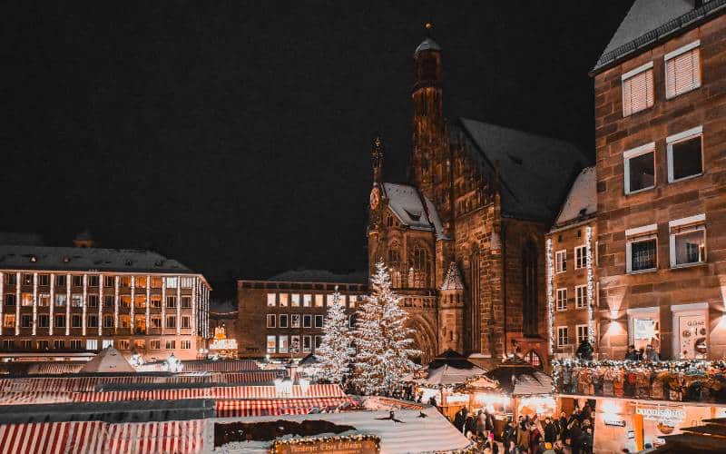 Nuremberg Christkindlesmarkt - Main market with Frauenkirche, two silver glowing Christmas trees in front of it, and red and white striped roofs on the market stalls - angiestravelroutes.com