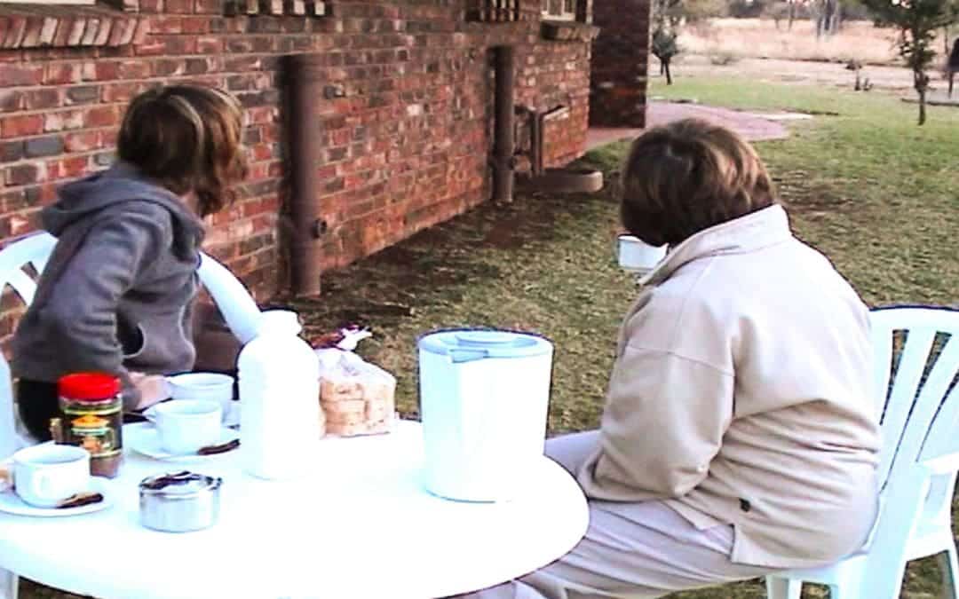 Pilanesberg National Park, South Africa - my two colleagues sit at the table in front of our cottage and turn their heads away to watch guinea fowl and ostriches roaming around the house, on the table coffee cups, a kettle, instant coffee, a packet of toast and an ashtray - angiestravelroutes.com