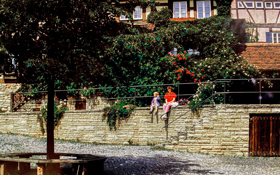 Sindelfingen, Old Town, 1992 - I (wearing a red blouse and red and white striped trousers) sit with Anna on a wall in Sindelfingen's Old Town, behind us an ivy-covered wall - angiestravelroutes.com