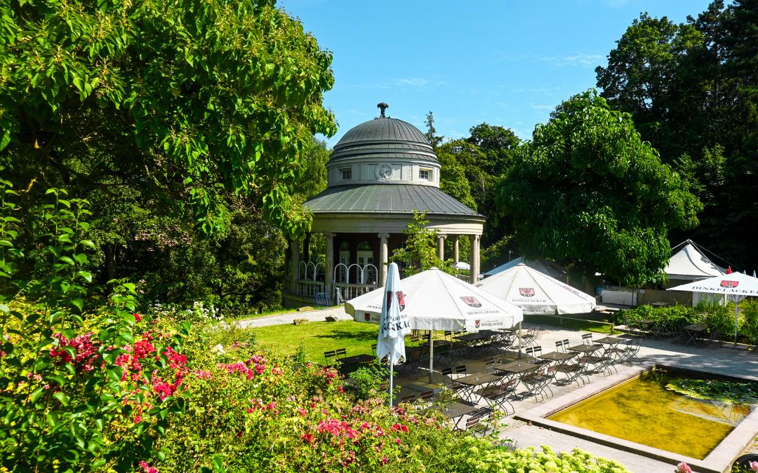 Weißenburgpark, Stuttgart - der Jugendstilpavillon davor der Biergarten mit großen weißen Sonnenschirmen, ilinks m Vordergrund einige Blumen der Parkbepflanzung - angiestravelroutes.com