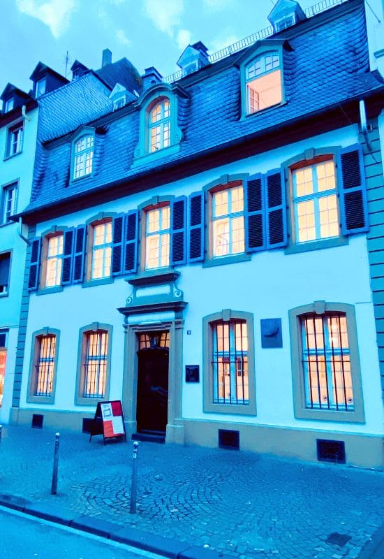 Barocke Fassade des Karl-Marx-Hauses mit beleuchteten Fenstern in der Trierer Brückenstraße am frühen Abend.