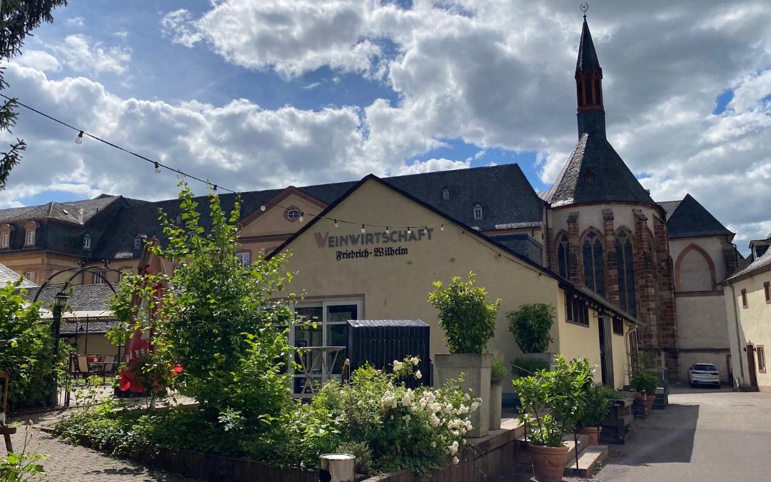 Außenansicht der Weinwirtschaft Friedrich Wilhelm mit Garten, im Hintergrund die Jesuitenkirche.
