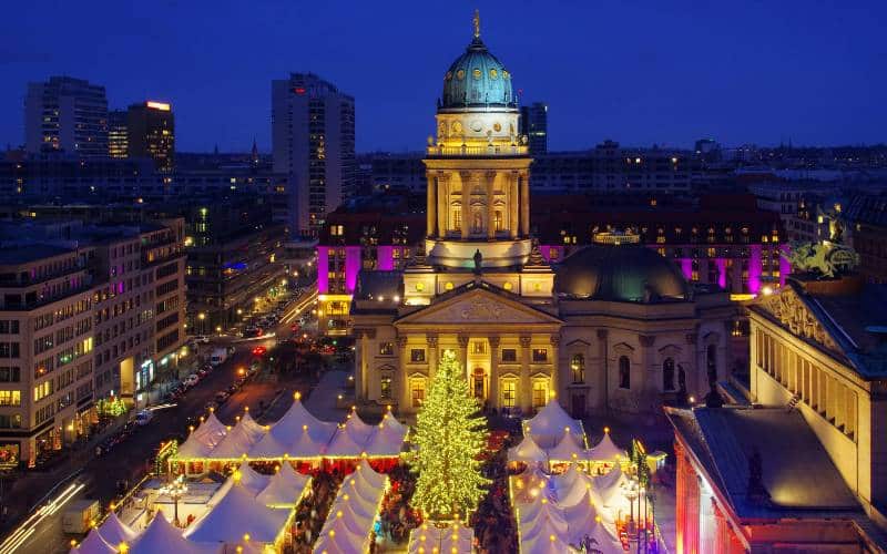Luftaufnahme Weihnachtsmarkt Gendarmenmarkt Berlin, Blick auf die spitzen weißen Dächer der Weihnachtsmarkthütten und den Deutschen Dom. - angiestravelroutes.com